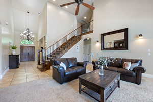 Living area with a towering ceiling, stairway, a ceiling fan, carpet, and a chandelier