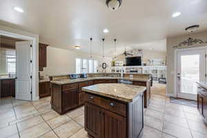Kitchen with a large island with sink, vaulted ceiling, light tile patterned floors, open floor plan, and hanging light fixtures