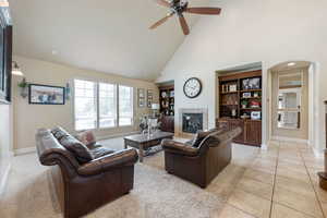 Living area with a high end fireplace, arched walkways, high vaulted ceiling, a ceiling fan, and light tile patterned floors