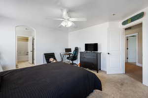 Bedroom featuring arched walkways, ceiling fan, connected bathroom, and light colored carpet