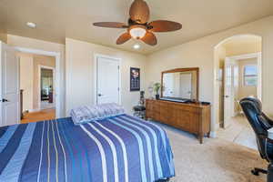 Bedroom featuring arched walkways, light carpet, and a ceiling fan
