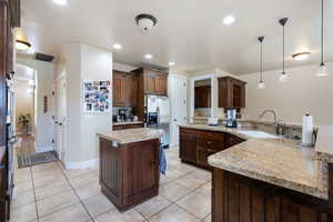 Kitchen featuring stainless steel fridge, a peninsula, decorative light fixtures, light tile patterned floors, and light stone counters