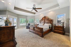 Carpeted bedroom with a tray ceiling, multiple windows, recessed lighting, access to outside, and a ceiling fan