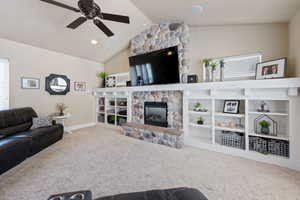 Living area featuring a fireplace, ceiling fan, vaulted ceiling, and carpet floors