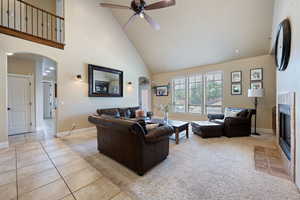 Living area with arched walkways, high vaulted ceiling, ceiling fan, tile patterned floors, and a fireplace