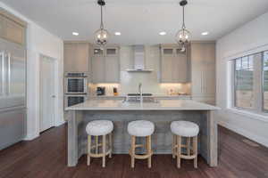 Kitchen with wall chimney range hood, double oven, built in fridge, a chandelier, and recessed lighting