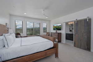 Bedroom with multiple windows, light colored carpet, recessed lighting, a barn door, and connected bathroom