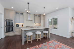 Kitchen featuring wall chimney exhaust hood, stainless steel appliances, gray cabinets, light countertops, and decorative backsplash