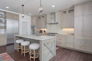 Kitchen featuring wall chimney exhaust hood, appliances with stainless steel finishes, light countertops, open shelves, and dark wood finished floors