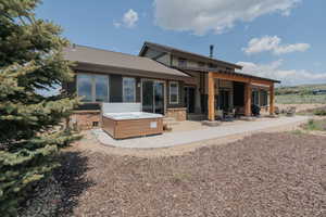 Back of house featuring a hot tub, a patio area, and a shingled roof