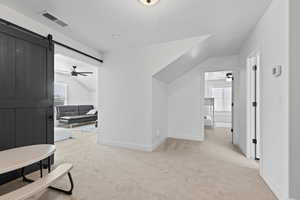 Hallway featuring light carpet, a barn door, healthy amount of natural light, and vaulted ceiling
