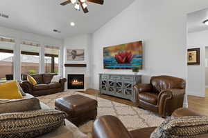 Living area featuring ceiling fan, wood finished floors, a tiled fireplace, high vaulted ceiling, and recessed lighting