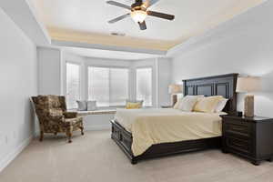 Bedroom featuring a tray ceiling, light colored carpet, multiple windows, and ceiling fan