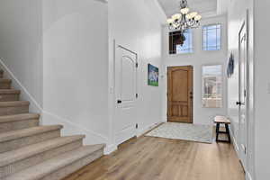 Foyer with stairway, a chandelier, light wood finished floors, a tray ceiling, and a towering ceiling