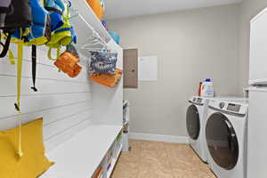 Laundry room featuring electric panel, washer and clothes dryer, and light tile patterned floors