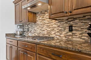 Kitchen featuring wall chimney exhaust hood, tasteful backsplash, stainless steel gas stovetop, and dark stone countertops