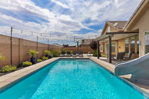 View of swimming pool with a water slide, a patio area, and a fenced backyard