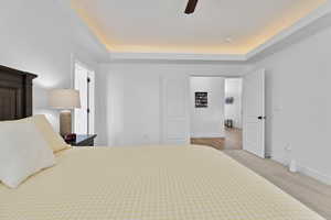 Bedroom with a raised ceiling, ceiling fan, and light carpet