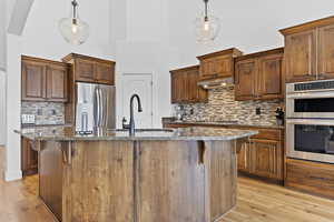 Kitchen featuring appliances with stainless steel finishes, dark stone countertops, light wood-style floors, tasteful backsplash, and a towering ceiling