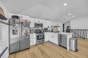 Kitchen with appliances with stainless steel finishes, vaulted ceiling, a peninsula, white cabinets, and light wood finished floors