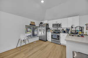 Kitchen featuring appliances with stainless steel finishes, white cabinetry, light wood-style floors, and high vaulted ceiling