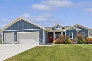 View of front facade featuring an attached garage, a front yard, concrete driveway, board and batten siding, and roof with shingles