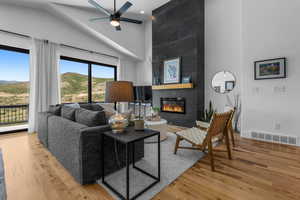 Living room featuring high vaulted ceiling, wood finished floors, a tile fireplace, ceiling fan, and a mountain view