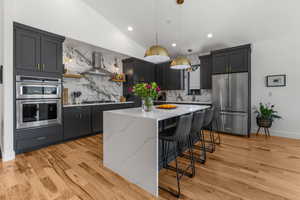 Kitchen featuring appliances with stainless steel finishes, wall chimney range hood, lofted ceiling, a kitchen island, and decorative backsplash