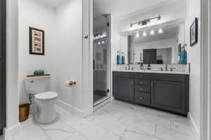 Full bath with marble look tile flooring, double vanity, a shower stall, and tasteful backsplash