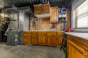 Kitchen featuring unfinished concrete floors, brown cabinetry, light countertops, and open shelves