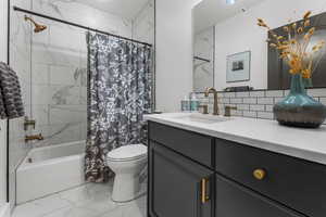 Bathroom featuring marble look tiles, vanity, shower / tub combo, decorative backsplash, and a chandelier