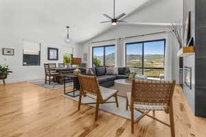 Living room with light wood finished floors, vaulted ceiling, a ceiling fan, a large fireplace, and a mountain view