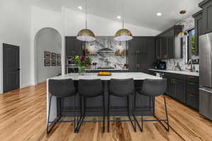 Kitchen with wall chimney exhaust hood, appliances with stainless steel finishes, light countertops, decorative backsplash, and light wood-style flooring