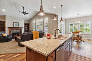 Kitchen featuring stainless steel dishwasher, healthy amount of natural light, light wood finished floors, a warm lit fireplace, and lofted ceiling