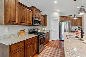 Kitchen featuring appliances with stainless steel finishes, dark wood-style flooring, light stone counters, recessed lighting, and decorative light fixtures