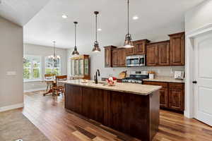 Kitchen featuring appliances with stainless steel finishes, wood finished floors, recessed lighting, light stone countertops, and a kitchen island with sink