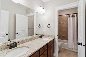 Bathroom with double vanity, shower / bath combo with shower curtain, and tile patterned flooring