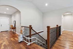 Hallway with an upstairs landing, arched walkways, wood finished floors, recessed lighting, and lofted ceiling