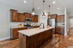 Kitchen with stainless steel appliances, arched walkways, dark wood finished floors, recessed lighting, and a center island with sink
