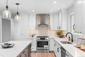 Kitchen featuring wall chimney range hood, appliances with stainless steel finishes, light stone counters, white cabinets, and recessed lighting