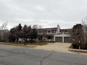 View of front of property with concrete driveway, a chimney, and an attached garage