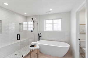 Bathroom featuring a freestanding bath, a stall shower, tile walls, recessed lighting, and a wainscoted wall