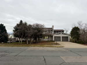 View of front facade with concrete driveway, a chimney, and a garage