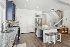 Kitchen featuring blue cabinetry, stainless steel appliances, a kitchen bar, wood finished floors, and recessed lighting