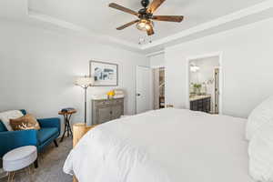 Carpeted bedroom featuring a raised ceiling, ensuite bathroom, and ceiling fan