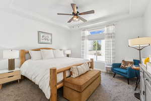 Carpeted bedroom featuring a raised ceiling and ceiling fan