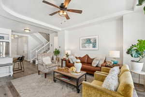 Living room featuring stairway, ceiling fan, wood finished floors, and a raised ceiling