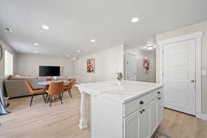 Kitchen featuring open floor plan, a kitchen island, light wood-type flooring, recessed lighting, and white cabinetry