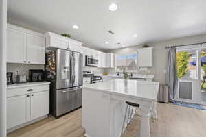 Kitchen featuring appliances with stainless steel finishes, light wood-type flooring, white cabinets, a center island, and plenty of natural light
