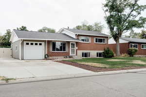 Tri-level home with an attached garage, driveway, brick siding, a shingled roof, and a gate